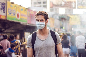 Fototapeta na wymiar Young handsome man walking around night market in Taipei with backpack and wearing a face pollution mask to protect himself from the coronavirus.