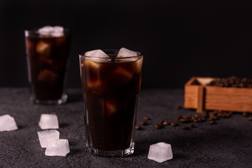 Iced coffee in a tall glass with cream poured over. Wood background. Low key.