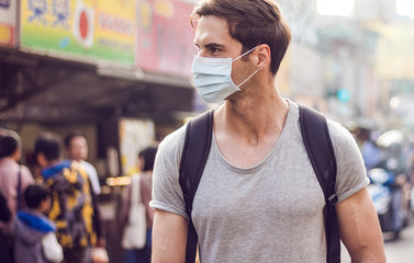 Young handsome man walking around night market in Taipei with backpack and wearing a face pollution mask to protect himself from the coronavirus.