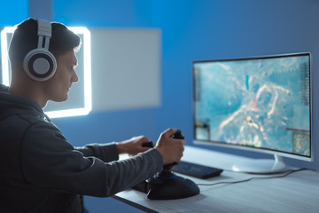 The gamer with headphones playing video games on the illuminated background © Artem