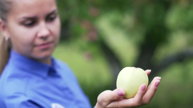 A young girl in a blue shirt looks at an apple in her hand.