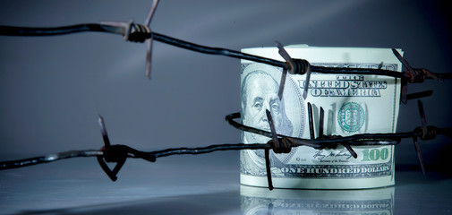 US Dollar bills wrapped in barbed wire as symbol of economic warfare, sanctions and embargo busting.