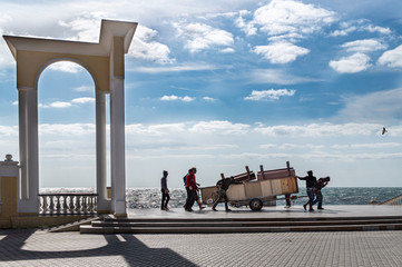 A group of men drag a heavy wagon along the seafront.