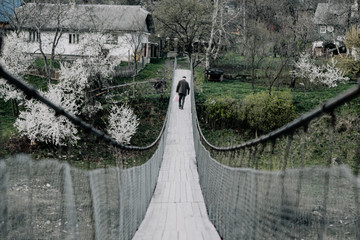 a cable bridge stretched between two river banks in a small mountain village, an old man crosses a bridge. The concept of loneliness, distance and poverty