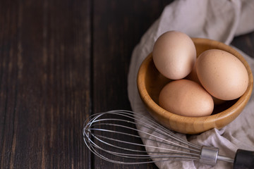 Raw chicken eggs with whisk on wooden background. Ready to start the cooking  concept
