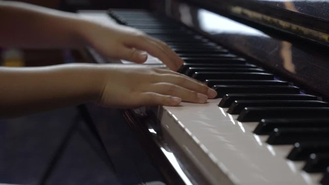 Close up child's hand playing piano at home, right up piano. Camera view is parallel to keyboard.
