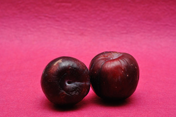 Two ripe plums on a pink background
