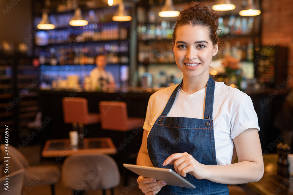 Wall mural young smiling waitress in apron and t-shirt standing in front of camera