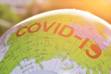 Blurred of globe with the red word "COVID-19" against the yellow sunrise background