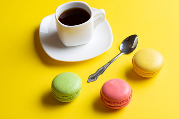 Colorful macarons with cup of coffee on yellow paper, flat lay