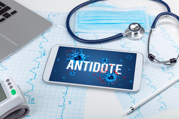 Tablet pc and doctor tools on white surface with ANTIDOTE inscription, pandemic concept