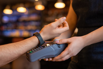 Hand of young client of cafe keeping arm with smartwatch over payment machine