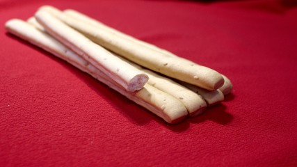 Bread cookie. Sweet bread sticks GRISSINI. Sweet sticks close up. Female hand takes bread sticks on a red background.