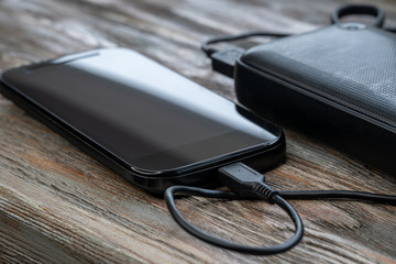 Mobile smart phones charging with energy bank on wooden desk.