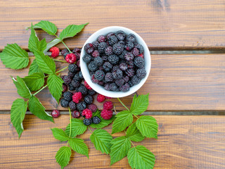 Cup of black juicy blackberry on a wooden background close-up with green leaves. View from above