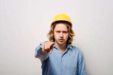 Frowning manual worker - builder, pointing with finger to you or camera, isolated on gray background, close-up studio shot.