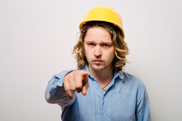 Frowning manual worker - builder, pointing with finger to you or camera, isolated on gray background, close-up studio shot.