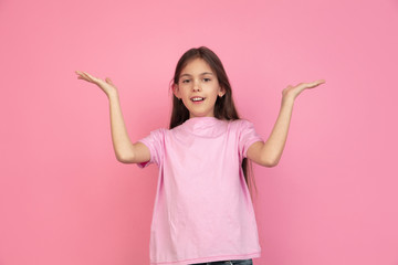Greeting, presenting. Caucasian little girl portrait isolated on pink studio background. Cute brunette model in shirt. Concept of human emotions, facial expression, sales, ad, childhood. Copyspace.