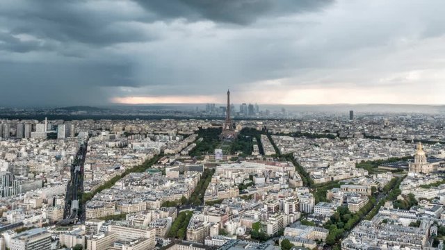 Aerial timelapse of storm clouds and rain in Paris over the Eiffel Tower as traffic builds on the streets and avenues below and construction cranes work on buildings.