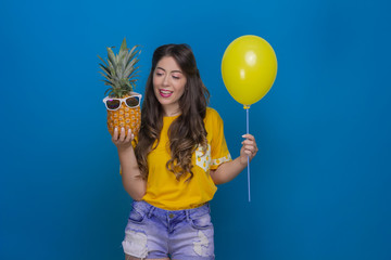 Happy girl holding a pineapple and a balloon on a blue background