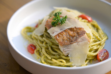 Spaghetti with Basil Pesto Sauce with grilled Asian seabass and Parmesan cheese slices on white plate.
