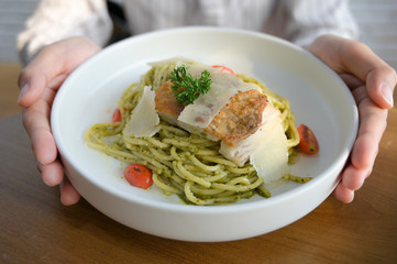 Spaghetti with Basil Pesto Sauce with grilled Asian seabass and Parmesan cheese slices on white plate in woman hands.