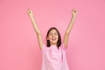 Celebrating win. Caucasian little girl portrait isolated on pink studio background. Cute brunette model in shirt. Concept of human emotions, facial expression, sales, ad, childhood. Copyspace.