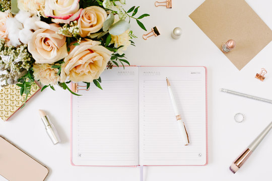 Feminine work space of blogger with beautiful bouquet of roses and opened notebook on white background. Mood and blogging concept. 