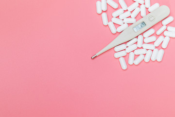 Digital thermometer and medicine pills with white bottle on pink background.