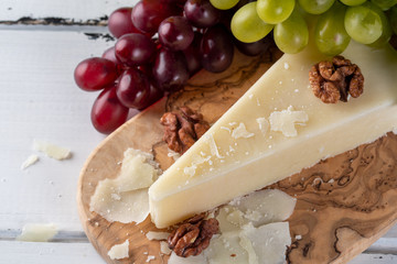 Pecorino romano, hard italian sheep milk cheese on wooden cutting board with grape, selective focus