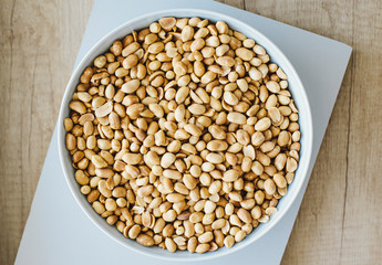 Peeled grains of peanuts in plate on wooden background. Top view. Cooking peanut butter.