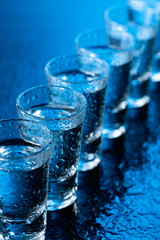Glasses of vodka on a damp glass table.