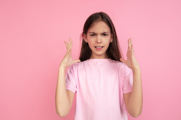 Angry. Caucasian little girl portrait isolated on pink studio background. Cute brunette model in shirt. Concept of human emotions, facial expression, sales, ad, childhood. Copyspace.