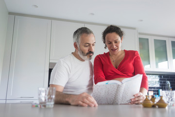 Happy pregnant woman with her husband sitting at home. Smiling couple consulting a book at the...