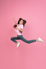 Jumping high. Caucasian little girl portrait isolated on pink studio background. Cute brunette model in shirt. Concept of human emotions, facial expression, sales, ad, childhood. Copyspace.