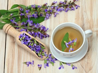 Sage herbal tea, Salvia officinalis. Sage leaves and flowers on wooden board. Focused on flowers in cup of tea