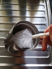 Closeup of lady using brush to wash her coffee glass in the kitchen. Household appliance concept.