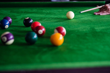 Man's hand and Cue arm playing snooker game or preparing aiming to shoot pool balls on a green billiard table. Colorful snooker balls on green frieze.