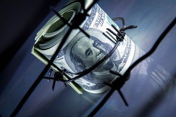Economic warfare, sanctions and embargo busting concept. Top view of US Dollar bills money wrapped in barbed wire.