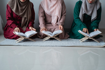 three young women wearing hijabs read the holy book of the Al-Quran together in the room