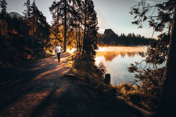 Trail runner in wild nature by lake, gold morning light in background