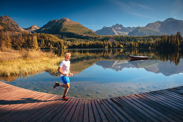 Young runner in beautiful clean autumn morning nature by lake under mountains