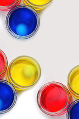 Three glass cans with blue yellow and red colorings for easter eggs proceeding on a linen tablecloth