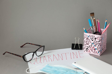  Quarantine. Business background. Medical mask, glasses, stationery, tablet, flowerpot on a bright grey background.