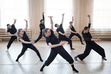 Three fit girls and four guys exercising with outstretched legs and bent knees