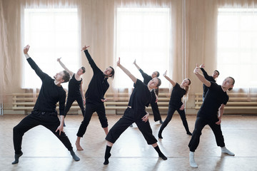 Group of young active dancers in black t-shirts and pants stretching one arm