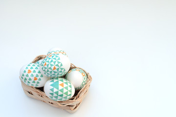 Decorated Easter eggs lie in the basket on white background. Happy Easter holiday concept. Greeting, invitation card. Flat lay style with copy space.