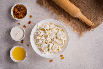 Cottage cheese in a white plate, separately honey, raisins on a white background. Healthy food. Top view.