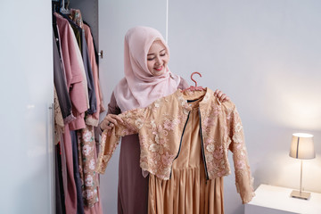 Asian hijab women measure a new gamis by the body in front the wardrobe in the room