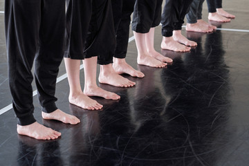 Row of legs of barefoot young dancers in black pants standing on the floor